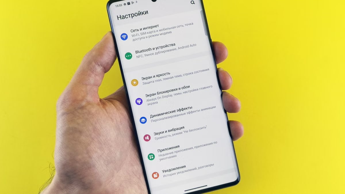 Close-up of a hand holding a smartphone with settings menu on a bright yellow background.